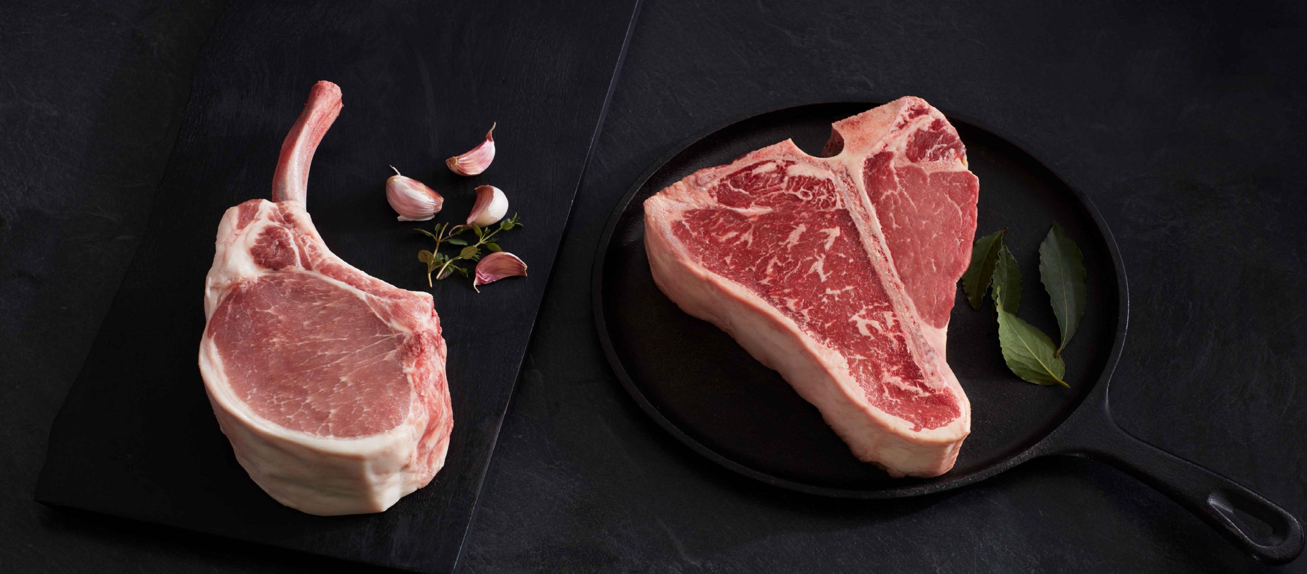raw bone-in pork chop and t-bone steak stylized on slate background