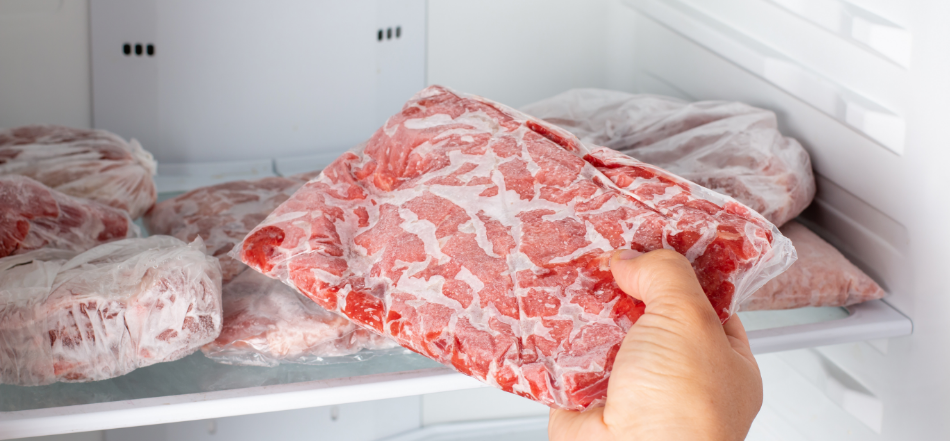A hand removes a vacuum-sealed package of ground beef from the other frozen meats in a home freezer