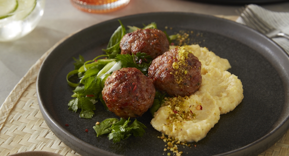 Spicy meatball appetizer made with ground beef and pork served with herb salad, potato puree and topped with a pistachio crumble.